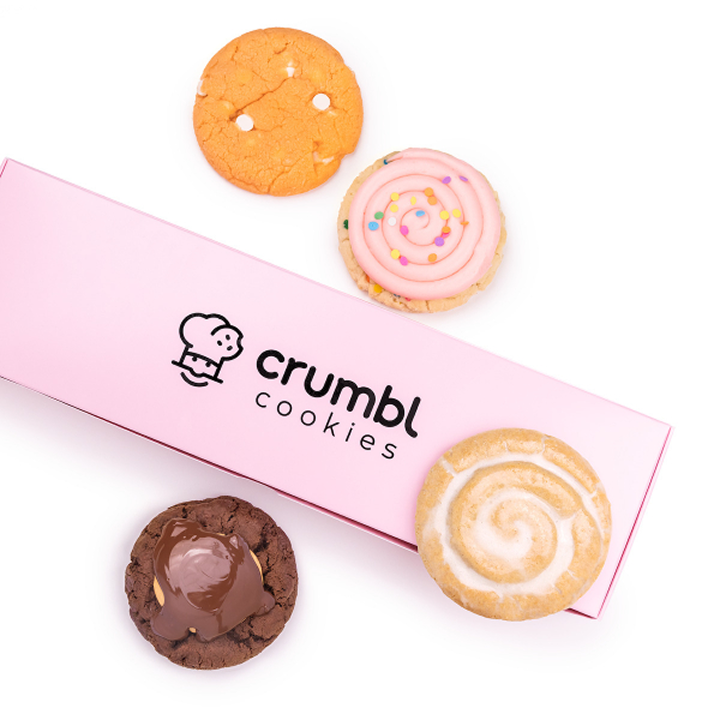 A closed box of Crumbl cookies with 4 different flavors around it.