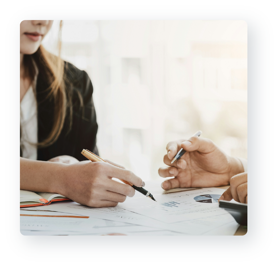 A woman using a pen to point to an area on a document and a man's hand following along.