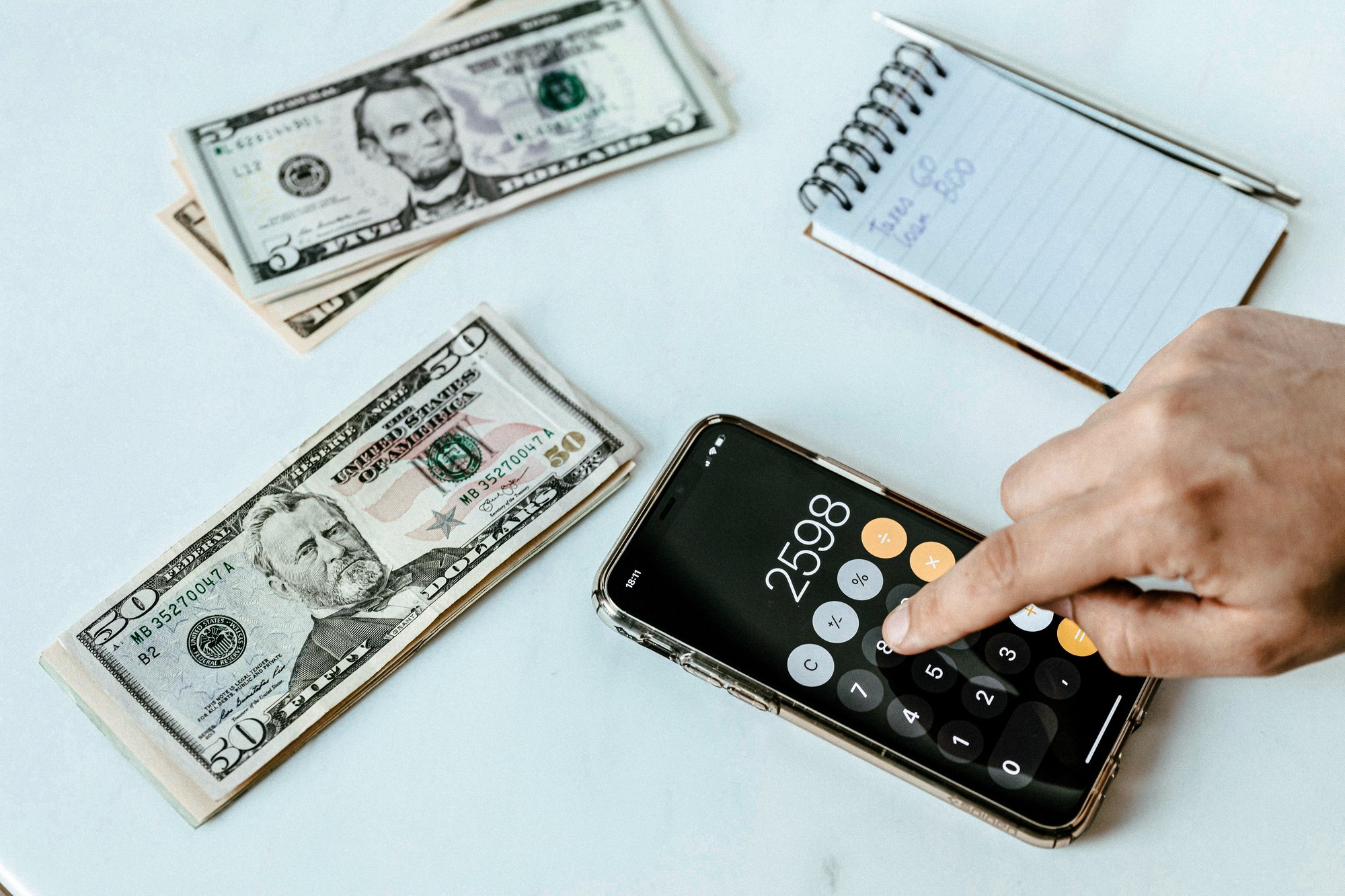 A hand using a calculator with a notepad and a few stacks of bills just above it.