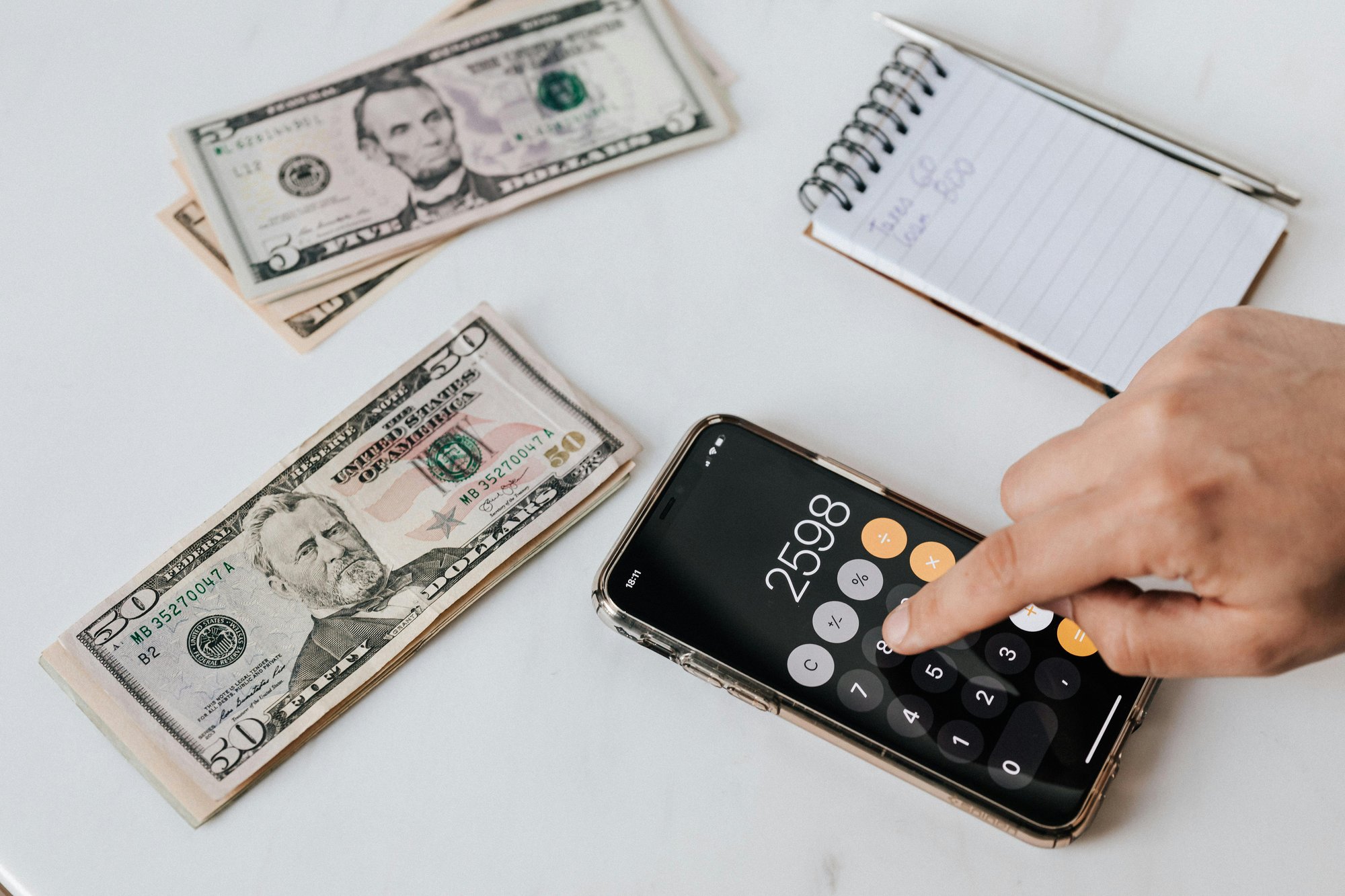 A hand using a calculator with a notepad and a few stacks of bills just above it.