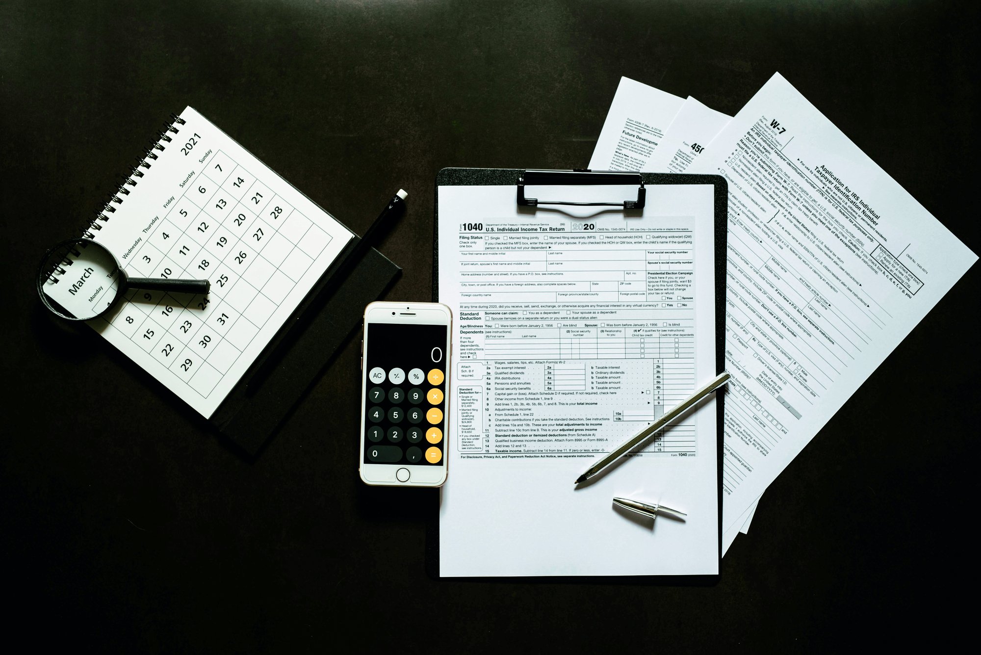 A clipboard full of tax documents with a calendar and calculator nearby.